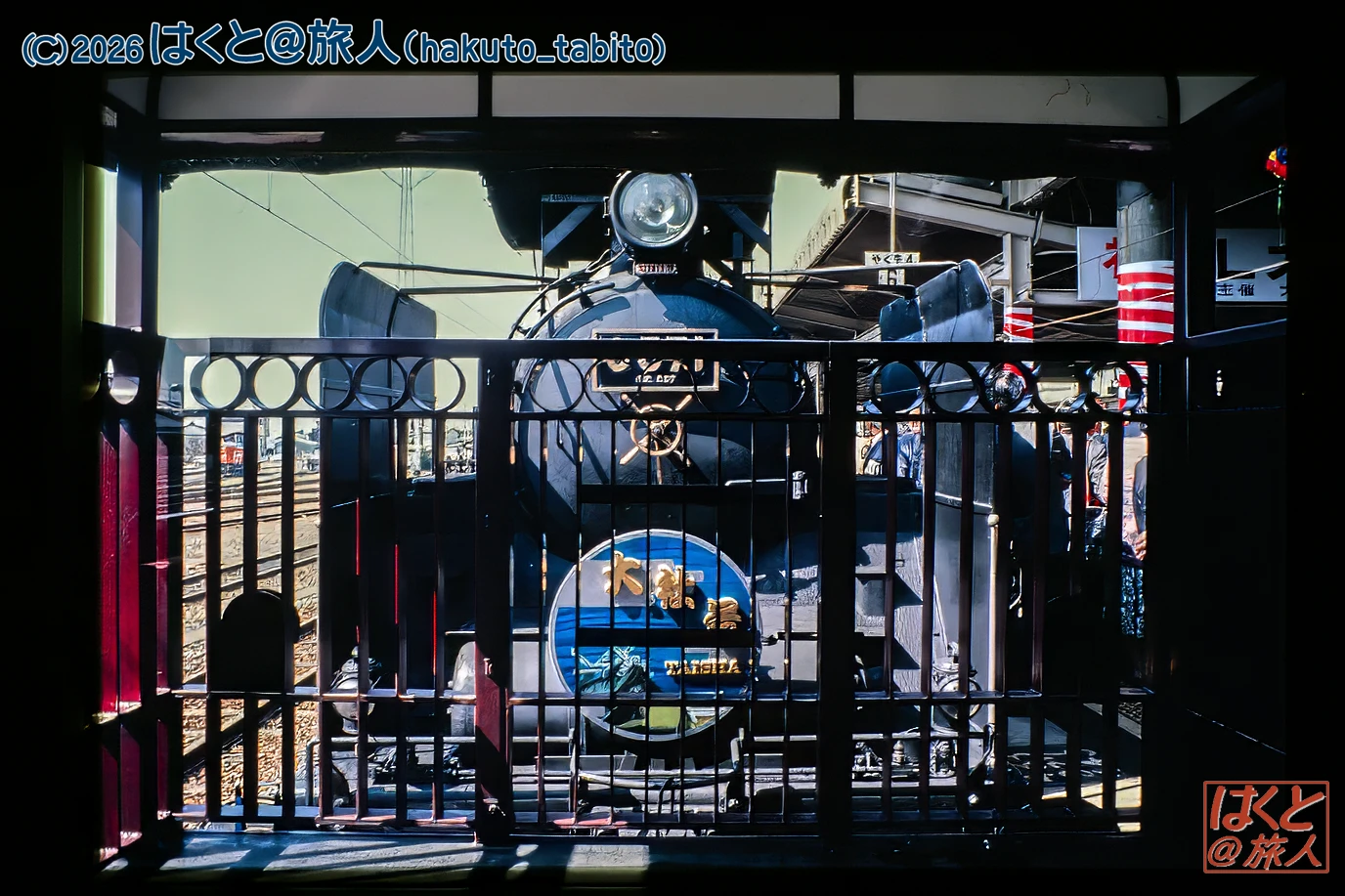 Blue steam locomotive seen through a decorative black gate at a train station.