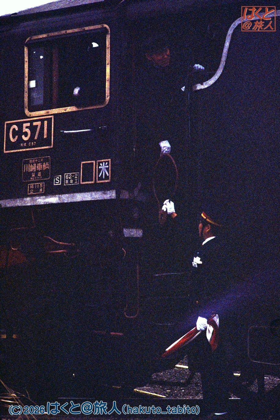 Night scene of a black steam locomotive marked C57 with a uniformed conductor inspecting near the side door.