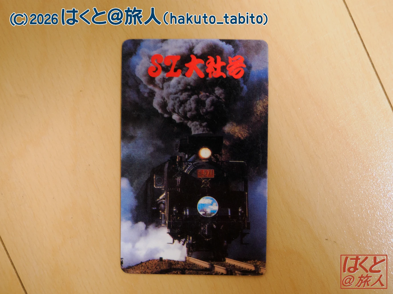 A black steam locomotive belching thick smoke, with red Japanese text above it on the card surface.