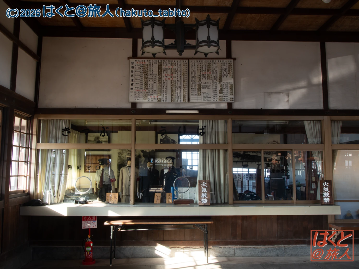 Interior of a vintage Japanese ticket counter with a large timetable board above, glass windows, and mannequins behind the counter.